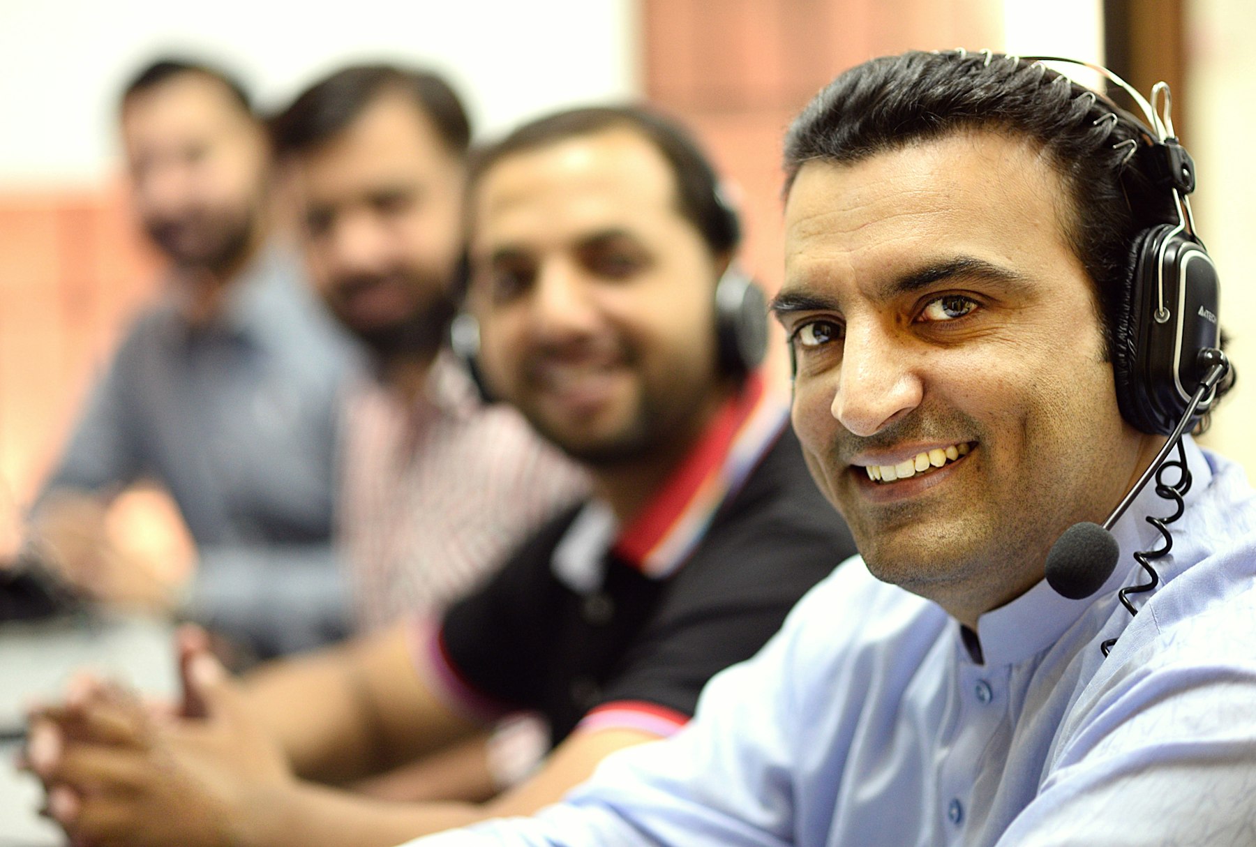 An Indian calling team wearing headsets, smiling at their desks