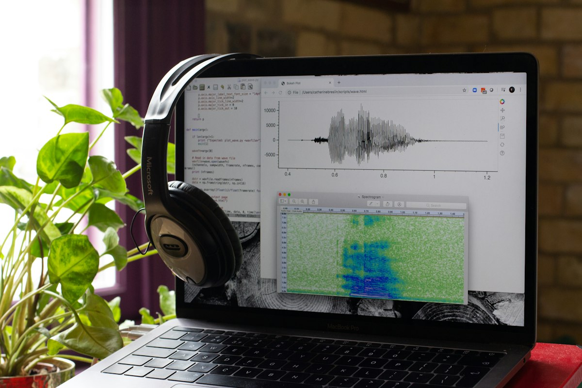A laptop showing a voice waveform, with a headset beside it